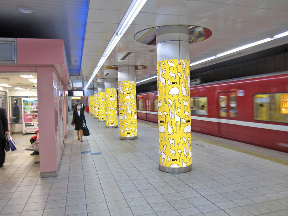 京急羽田空港第1・第2ターミナル駅ホーム、多くの乗客が行き交う導線上に掲出される、大型プリント出力シートで巻いた柱全周・全面を広告として使用できる、ユニークな媒体